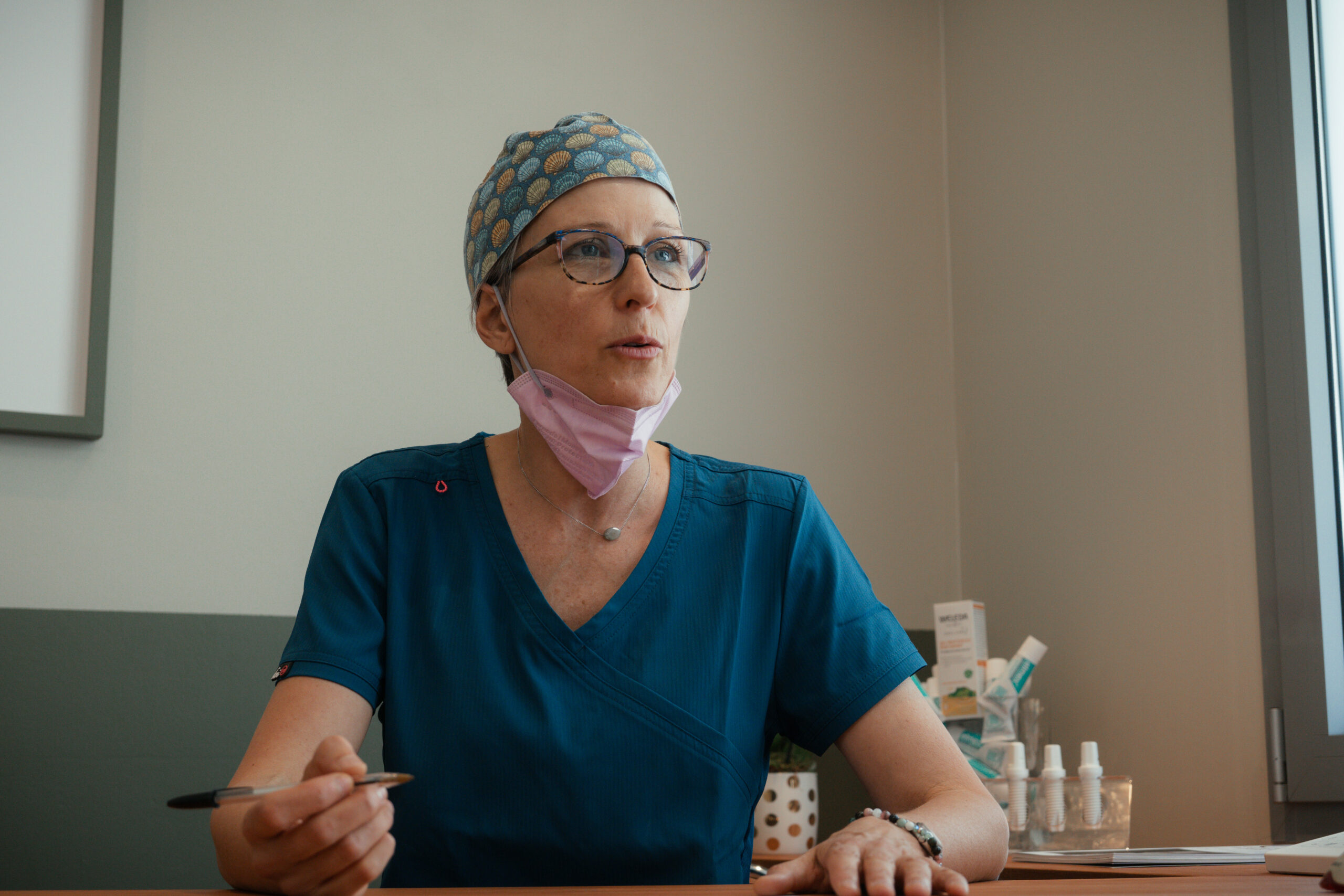 Dr Stéphanie Gouiran en blouse bleue, en consultation, tenant un stylo et écoutant un patient dans son cabinet à Carry-le-Rouet.